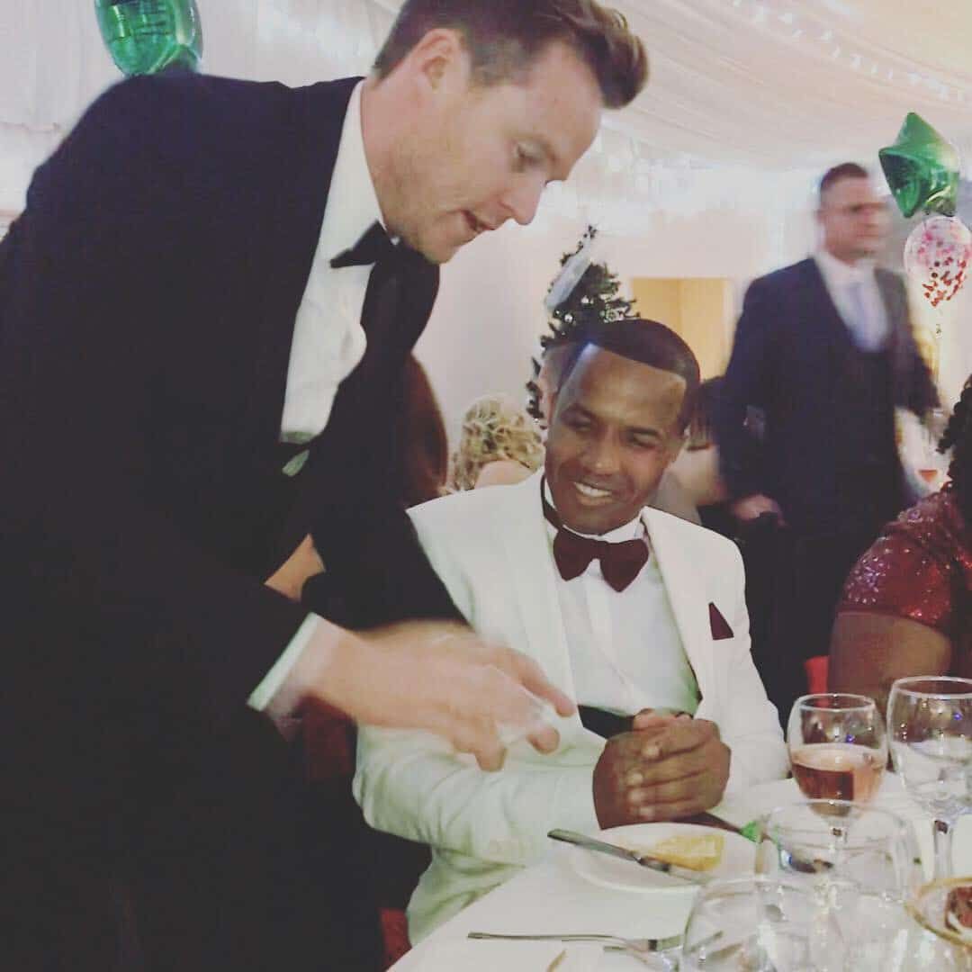 A guest in a white dinner jacket grinning as a trick unfolds at his table