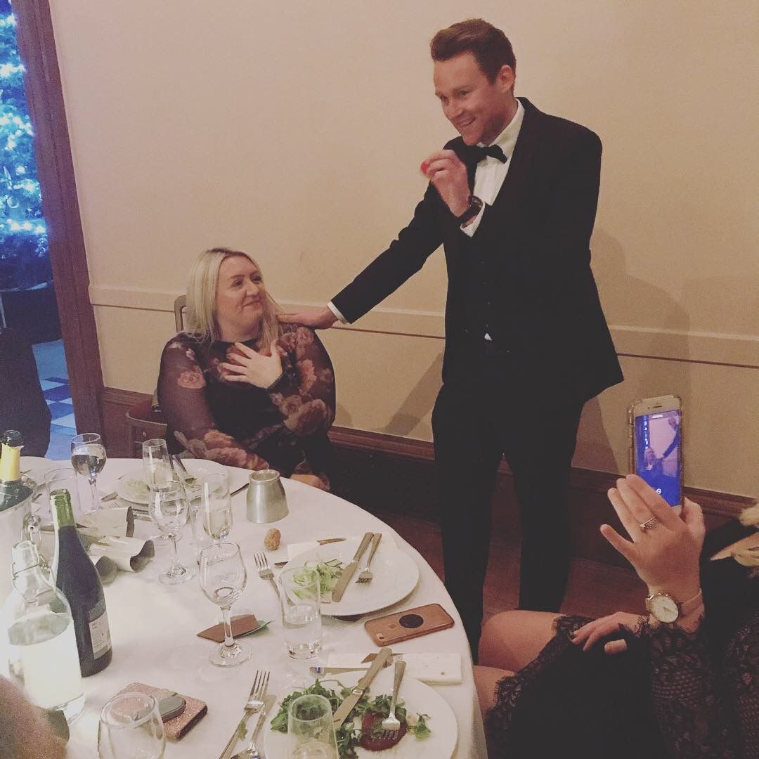 A guest with her hand on her chest in disbelief during magic at a black-tie dinner