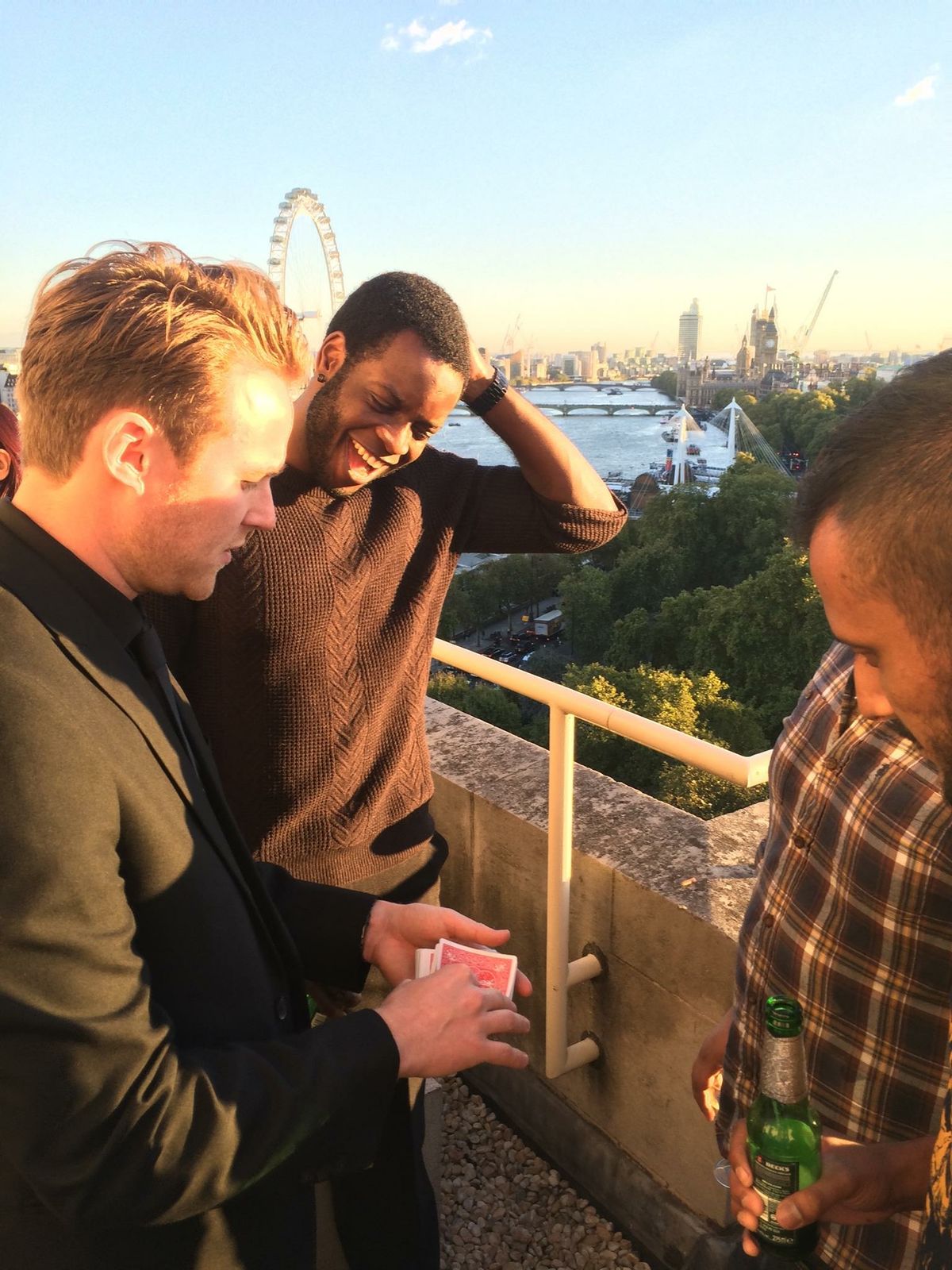 Richard Kettle performing a card trick for guests on a rooftop terrace overlooking London