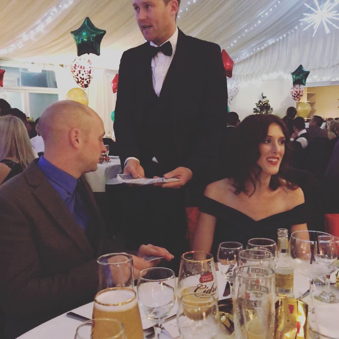 Guests laughing during close-up magic at a black-tie Christmas party