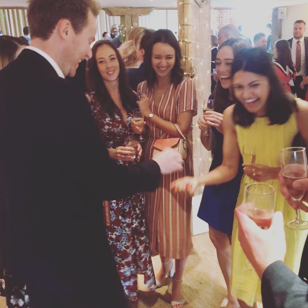 Guests with drinks in hand laughing as a card trick lands at a reception