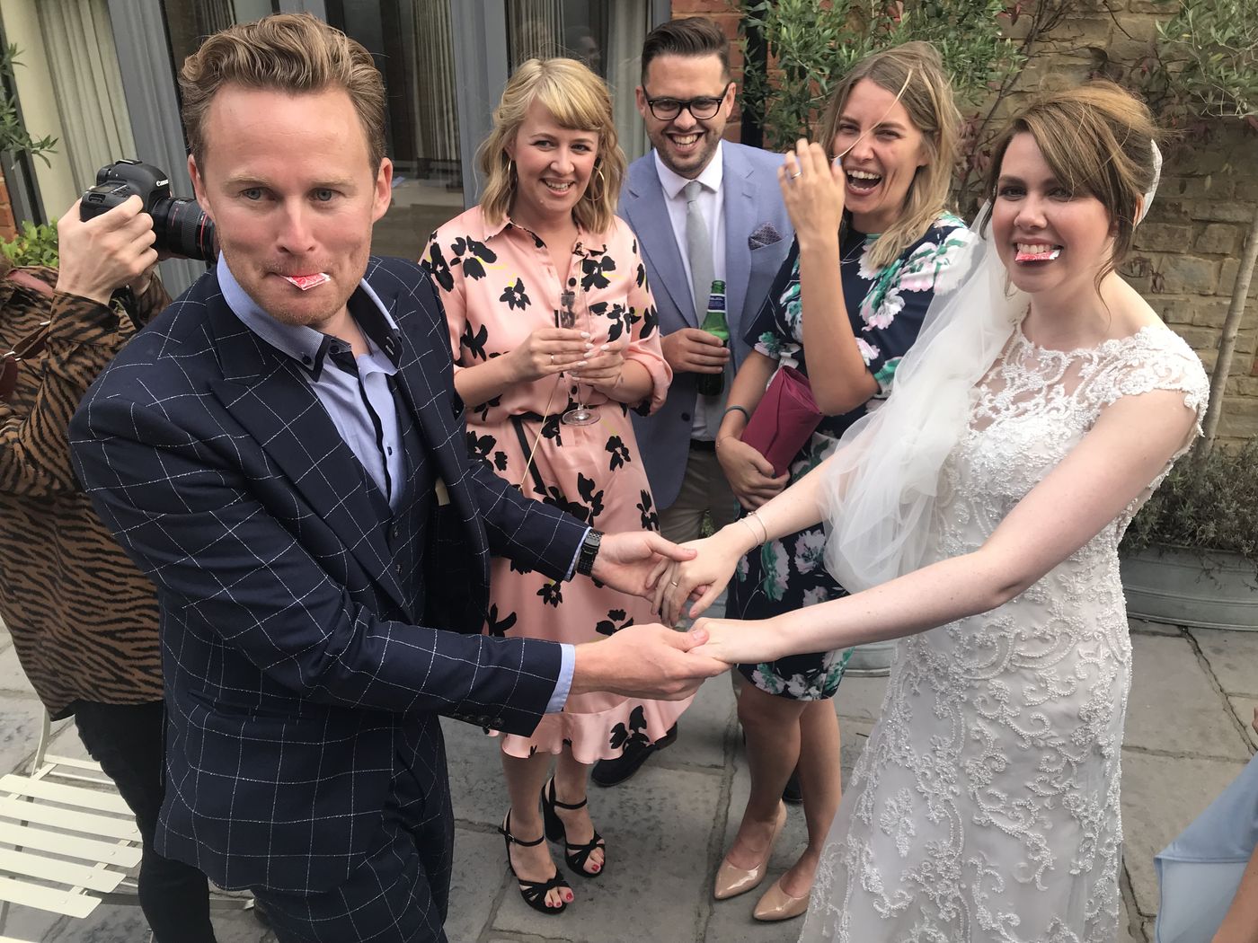 A bride and wedding guests laughing with playing cards held in their mouths during close-up magic