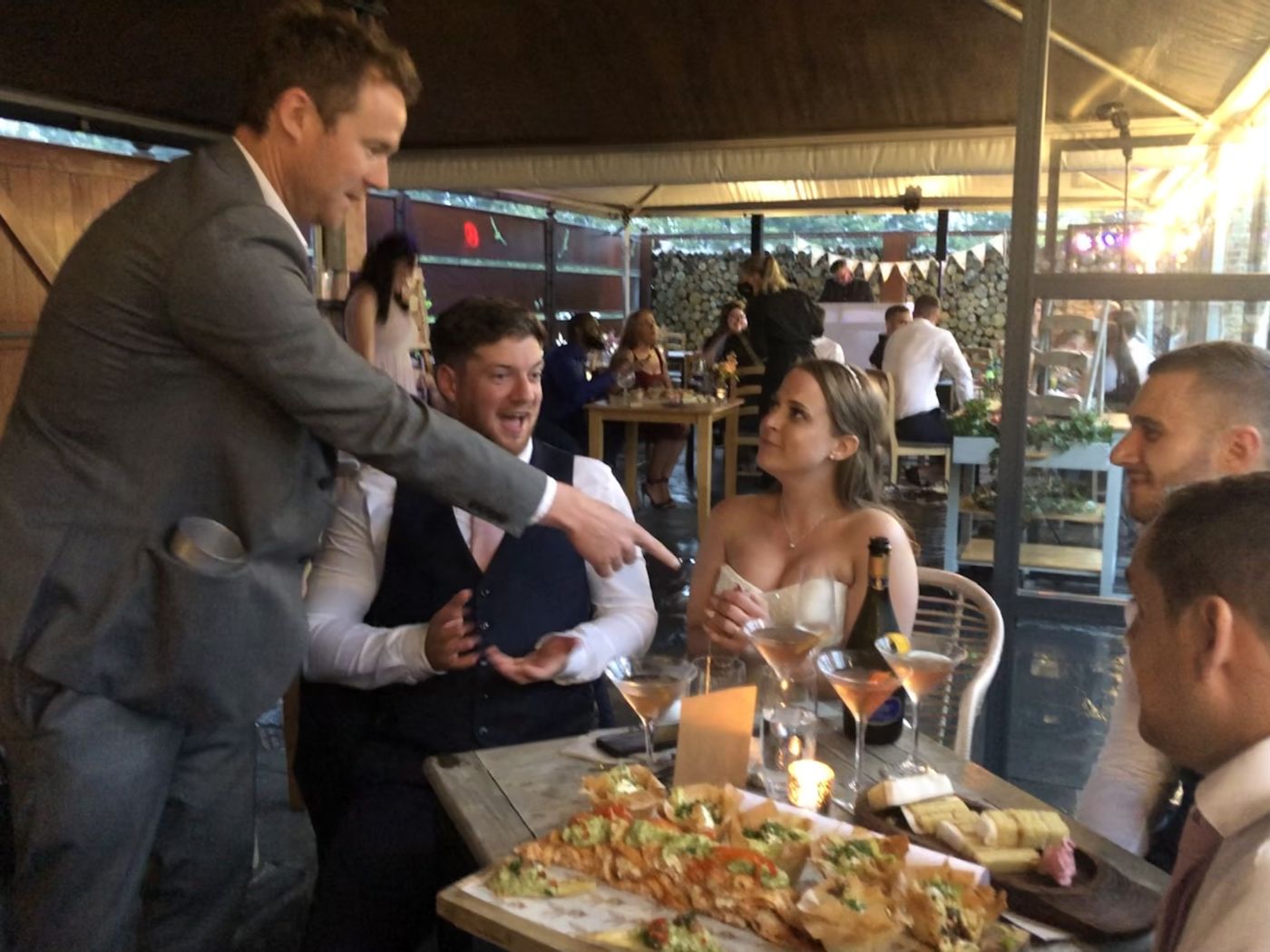 A groom reacting in disbelief to a close-up card trick at his wedding reception