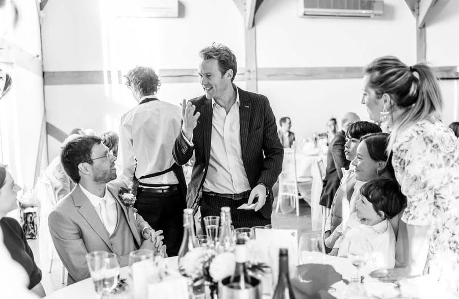 A groom laughing during close-up magic at his wedding reception
