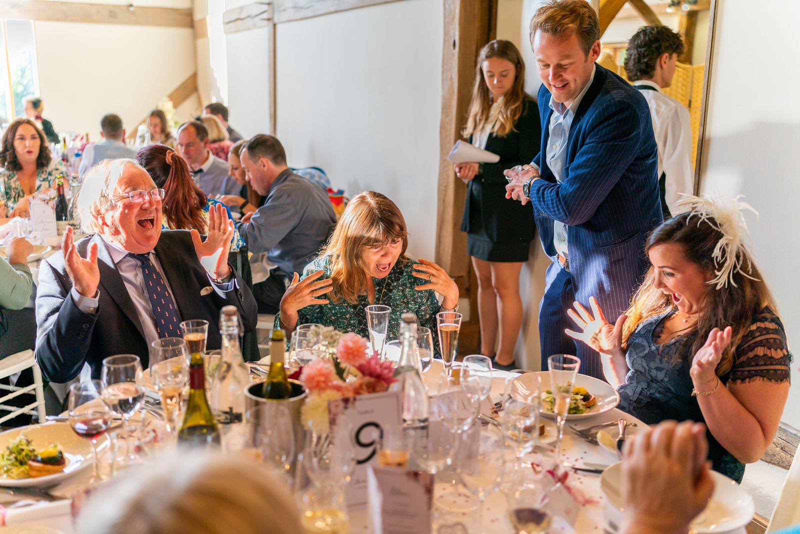 Wedding guests throwing their hands up in amazement at a barn reception table
