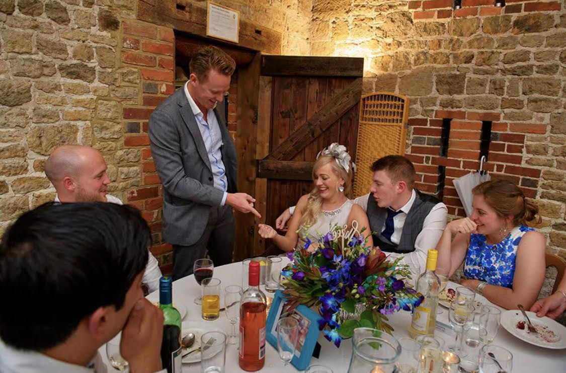 Richard Kettle performing a card trick for a wedding table in a stone barn