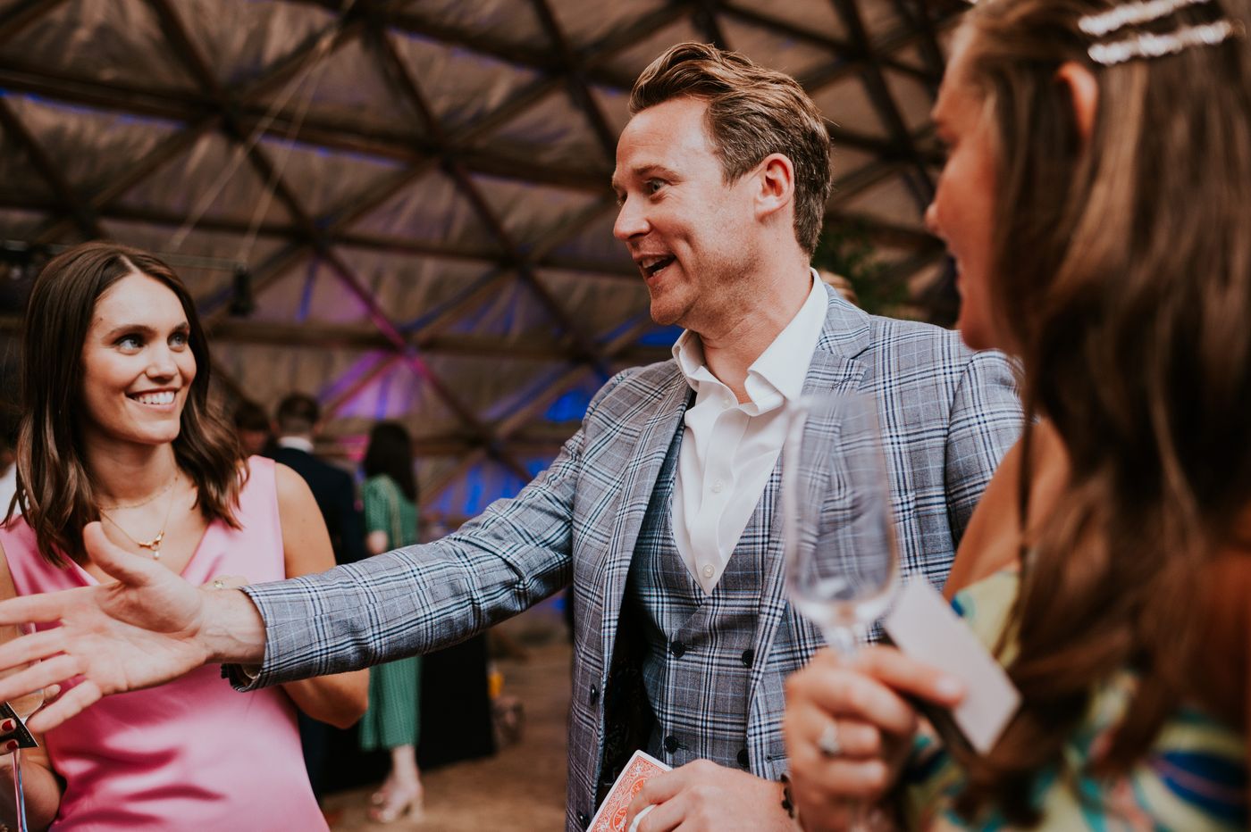 Richard Kettle revealing a card to a smiling guest at an evening wedding party